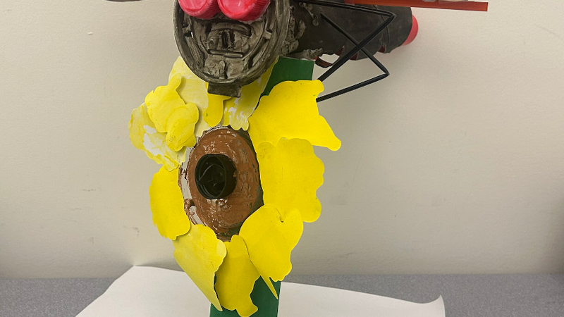 A dragonfly on top of a sunflower. Both were made of recycled materials.