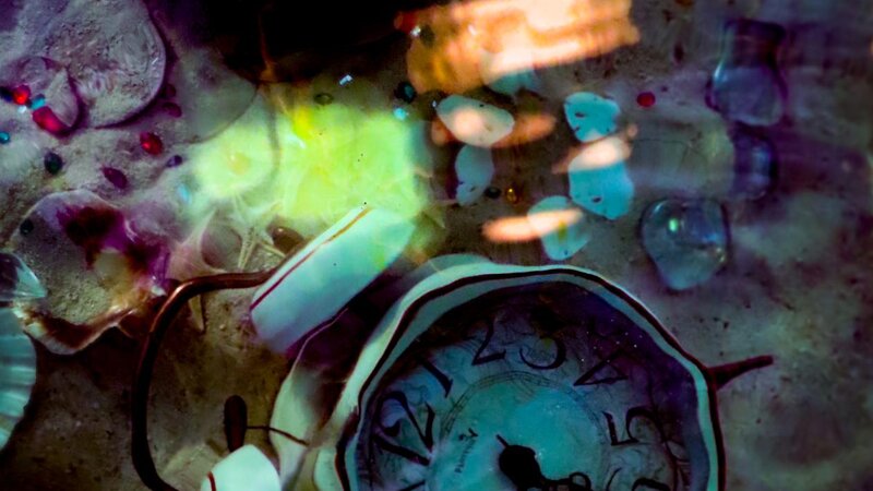 Clock sits on the bottom of the ocean surrounded by sand and treasures lost in time. 