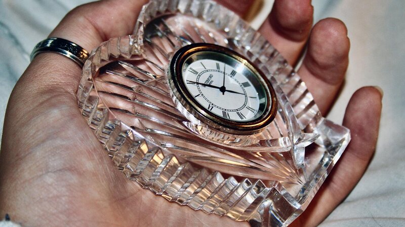 A cold colored hand losing grip with a heart shaped glass clock rested the palm of a hand. 