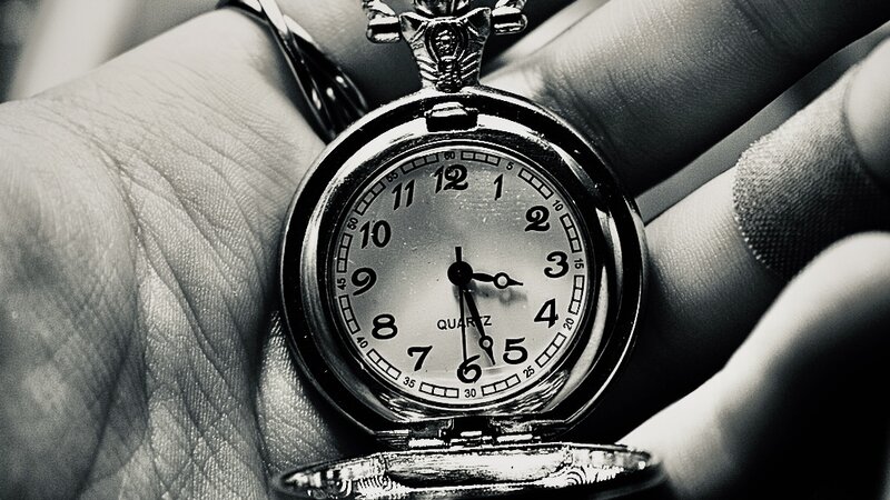 A black and white depiction of a hand holding “time” an open pocket watch 