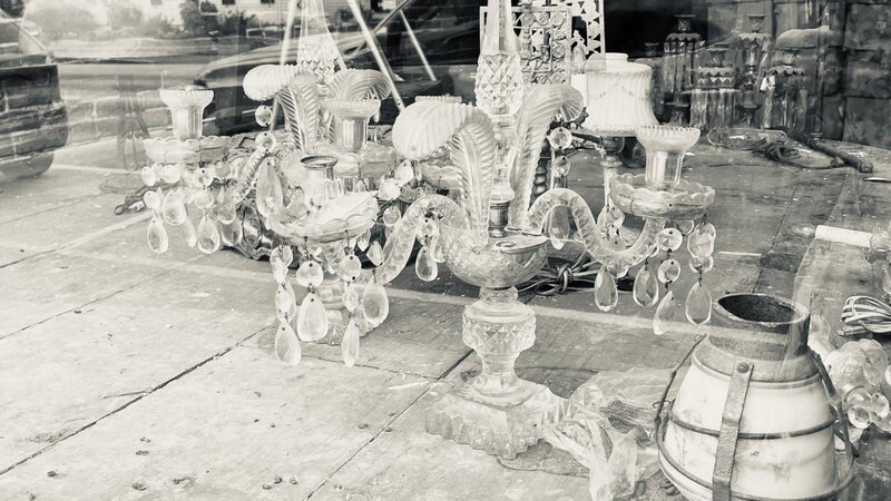 assorted antiques in the shop window messily arranged. This image is in black and white.