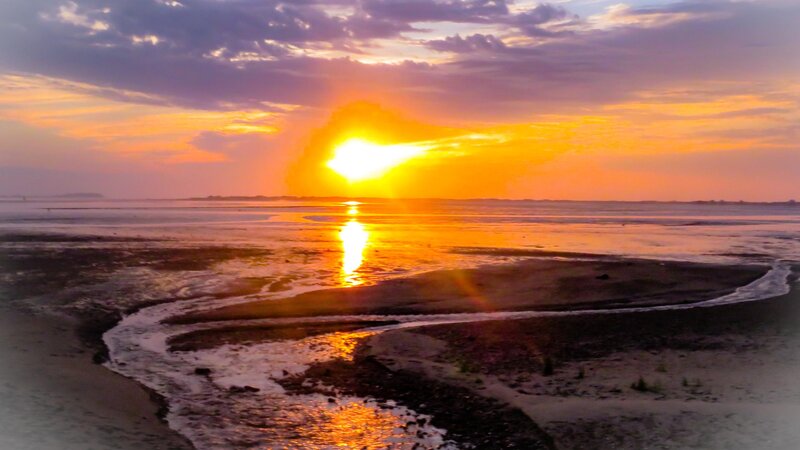 Sunrises over Nelson Beach in Plymouth, Massachusetts. The sun can be seen reflecting in the pools of water running to the ocean. 
