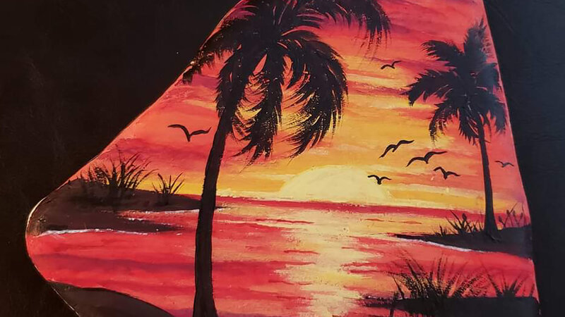 Image of red and gold sunset with sun, two palm trees and seagulls, painted on Santorini stone.
