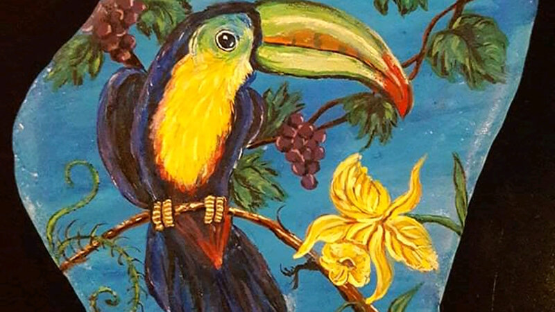 Colorful toucan, berries and flowers painted on Santorini stone.