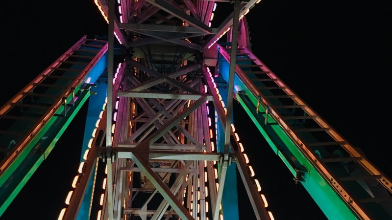 A view of the lit-up structure of the ferris wheel at night while riding the ferris wheel
