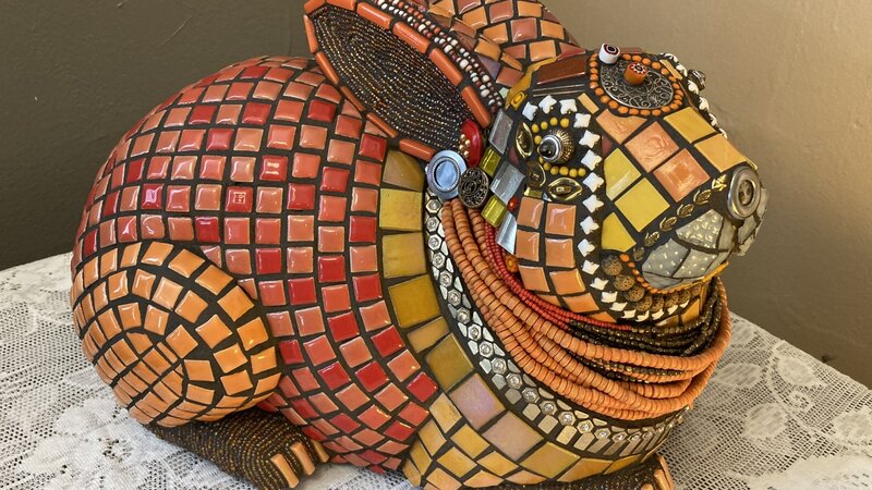 rabbit sculpture covered in red, orange, white, and metal tesserae