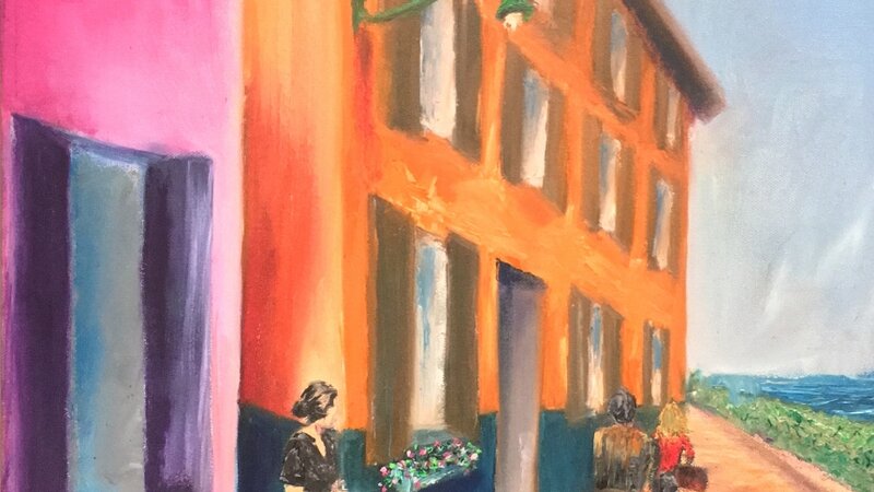 A woman watching people pass as she leans between two colorful buildings.