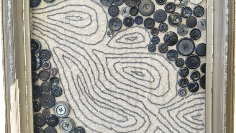 An old frame with some old buttons sewn on, and a river flowing through