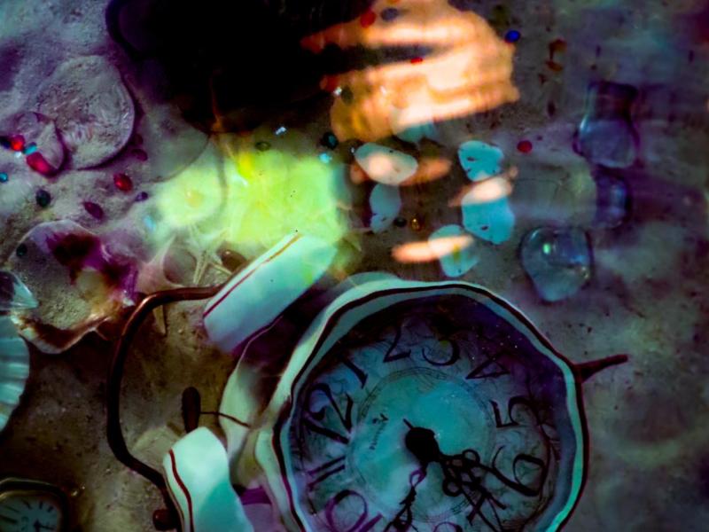 Clock sits on the bottom of the ocean surrounded by sand and treasures lost in time. 