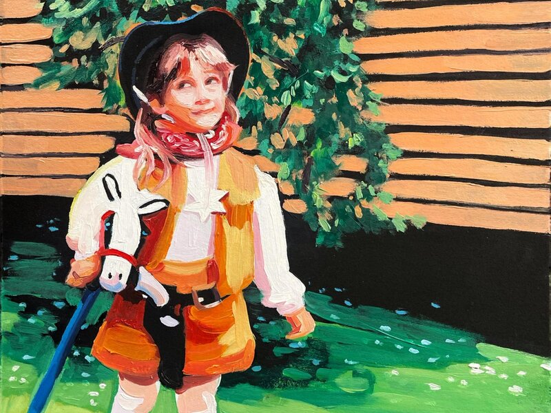A little girl dressed like a cowgirl, looking up to the left. The background is a simple mix of greenery and siding on a house. 