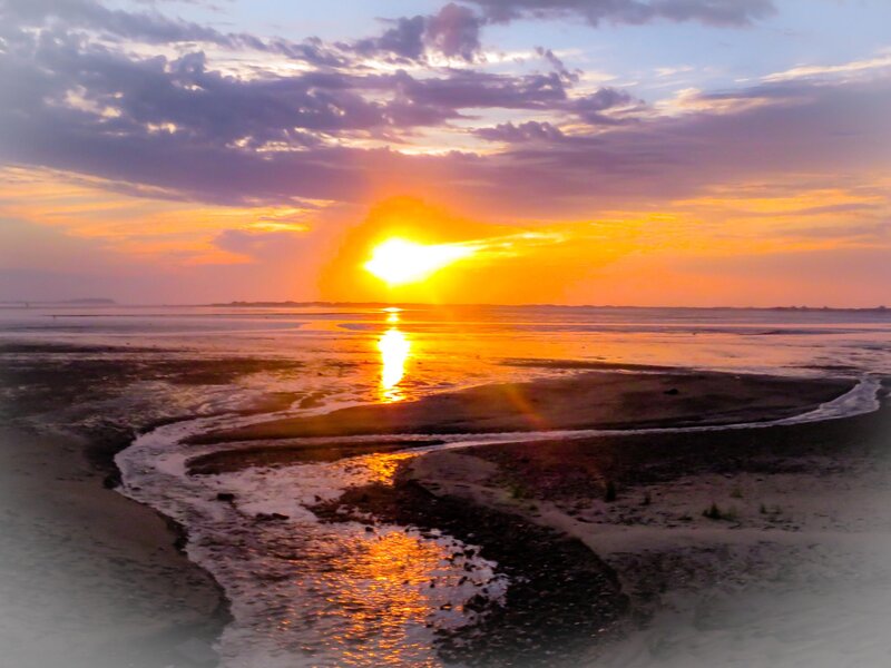 Sunrises over Nelson Beach in Plymouth, Massachusetts. The sun can be seen reflecting in the pools of water running to the ocean. 