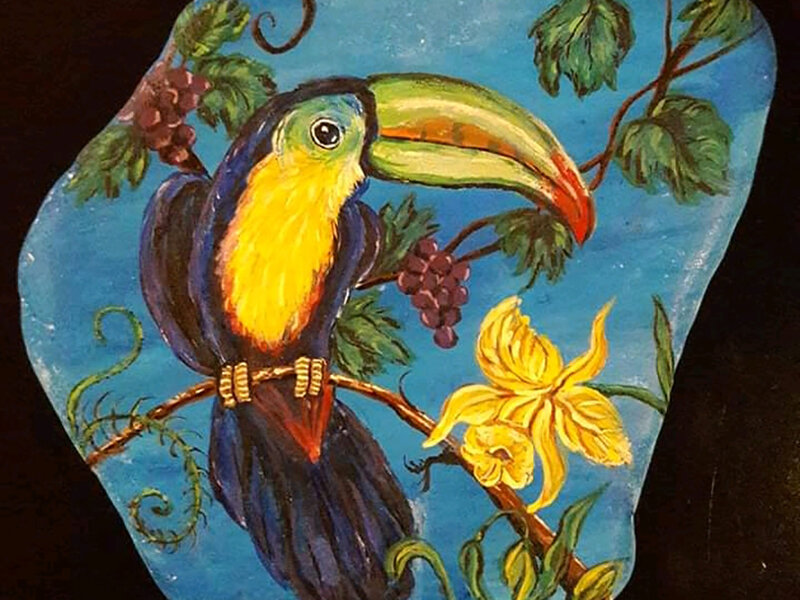 Colorful toucan, berries and flowers painted on Santorini stone.