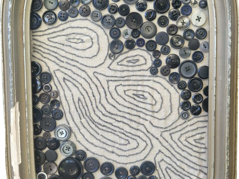 An old frame with some old buttons sewn on, and a river flowing through