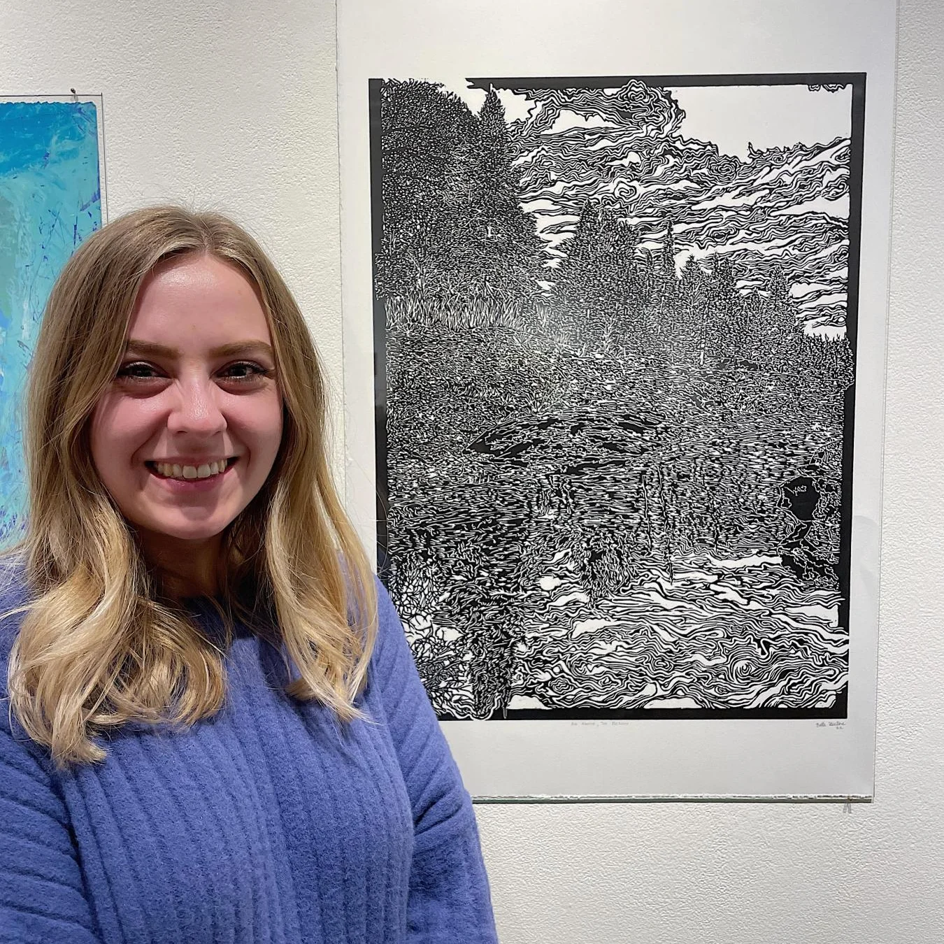 Belle Hulne standing in front of her relief print displayed on the gallery wall at Highpoint Center for Printmaking