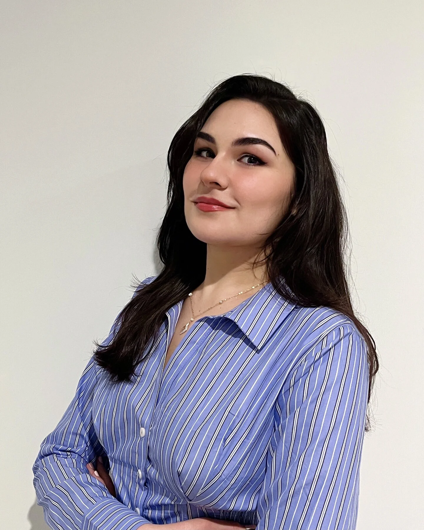 Photo of a young woman with long black hair wearing a blue button down shirt.