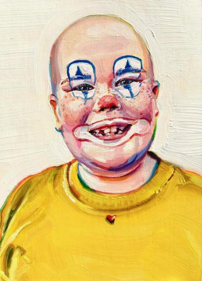 A young boy in a yellow shirt with clown makeup. He's bald and is missing teeth. The paint is chunky and colorful. 