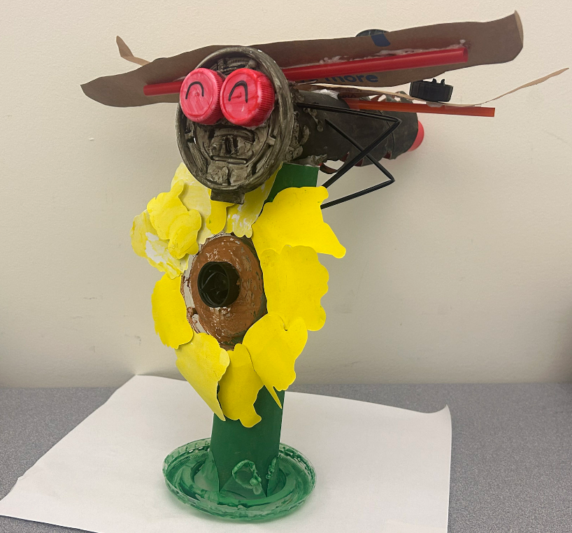 A dragonfly on top of a sunflower. Both were made of recycled materials.