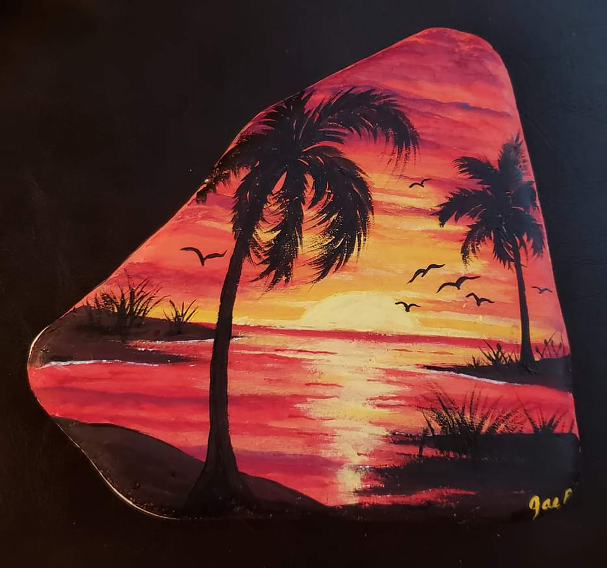 Image of red and gold sunset with sun, two palm trees and seagulls, painted on Santorini stone.